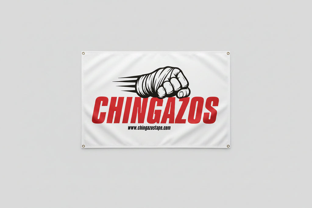 A white rectangular banner hanging on a concrete wall, printed with large red vertical text reading 'CHINGAZOS,' a black-and-white illustrated fist with claws, and small black website text. The banner has metal grommets at the corners.
