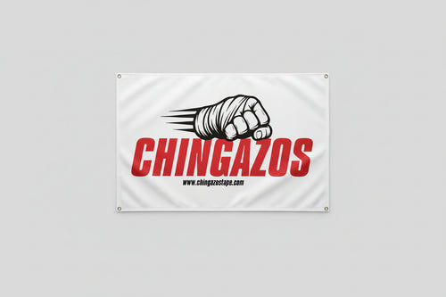 A white rectangular banner hanging on a concrete wall, printed with large red vertical text reading 'CHINGAZOS,' a black-and-white illustrated fist with claws, and small black website text. The banner has metal grommets at the corners.